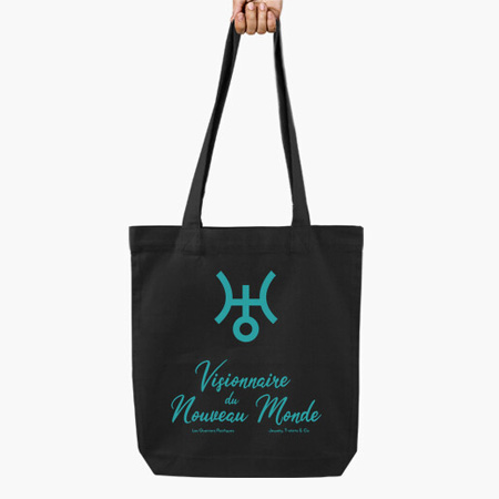 photographie d'une main qui tient un Totebag noir avec le symbole de la planète Uranus et l'inscription Visionnaire du Nouveau Monde en bleu turquoise